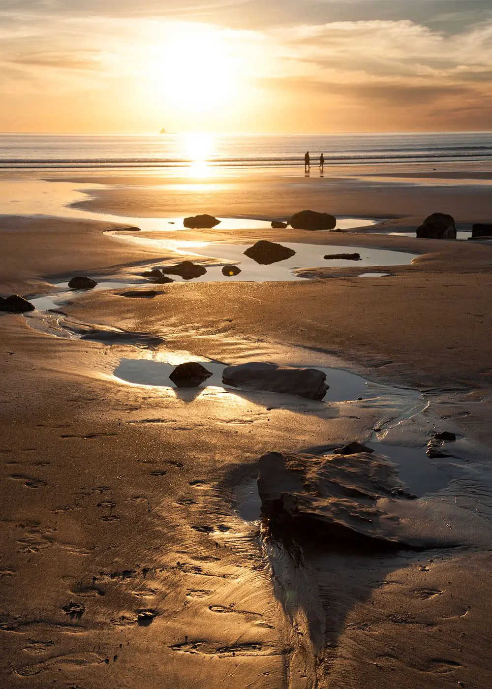 Sun setting over a beach with rocks and puddles on it