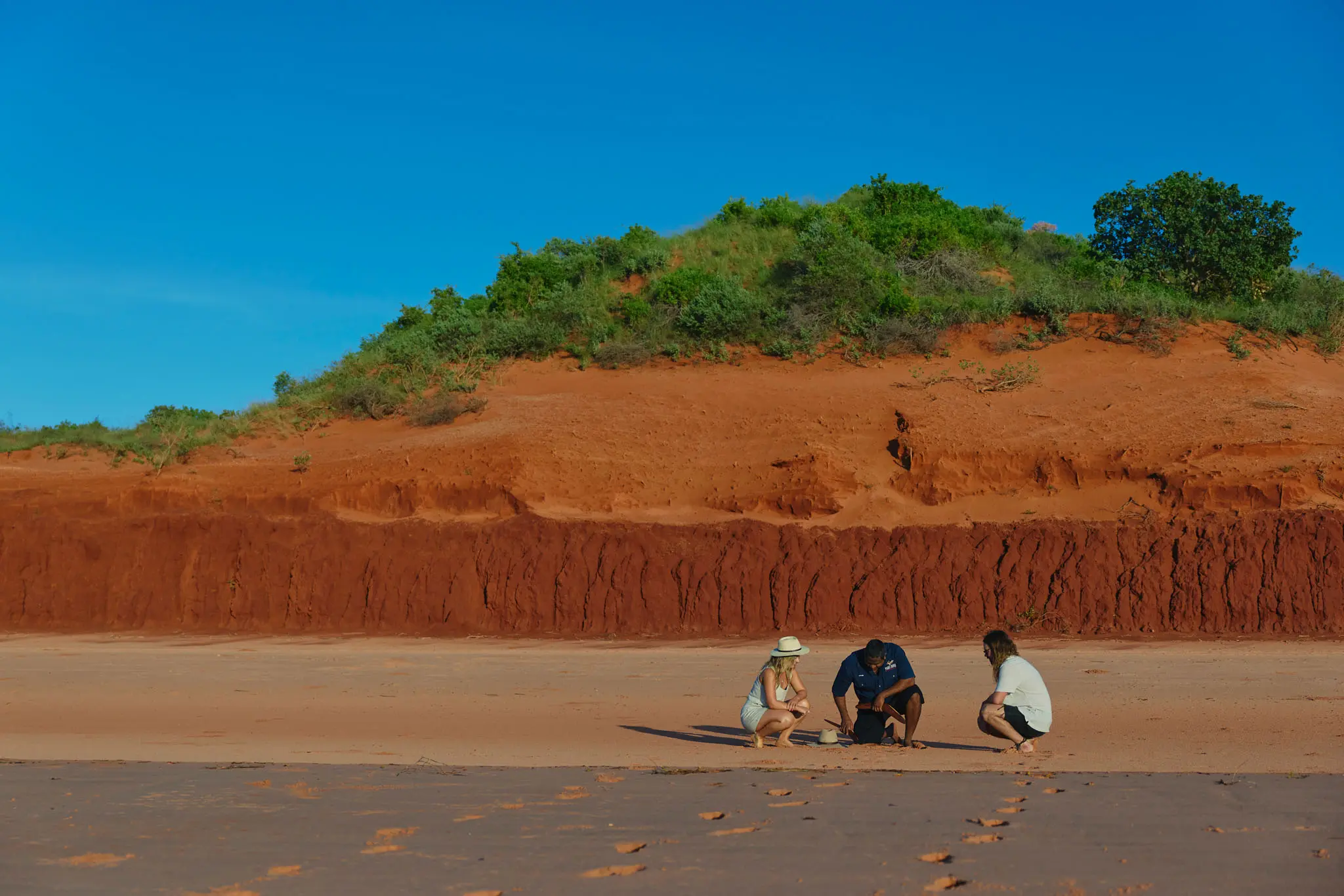 Three people crouching on a beach in Broome