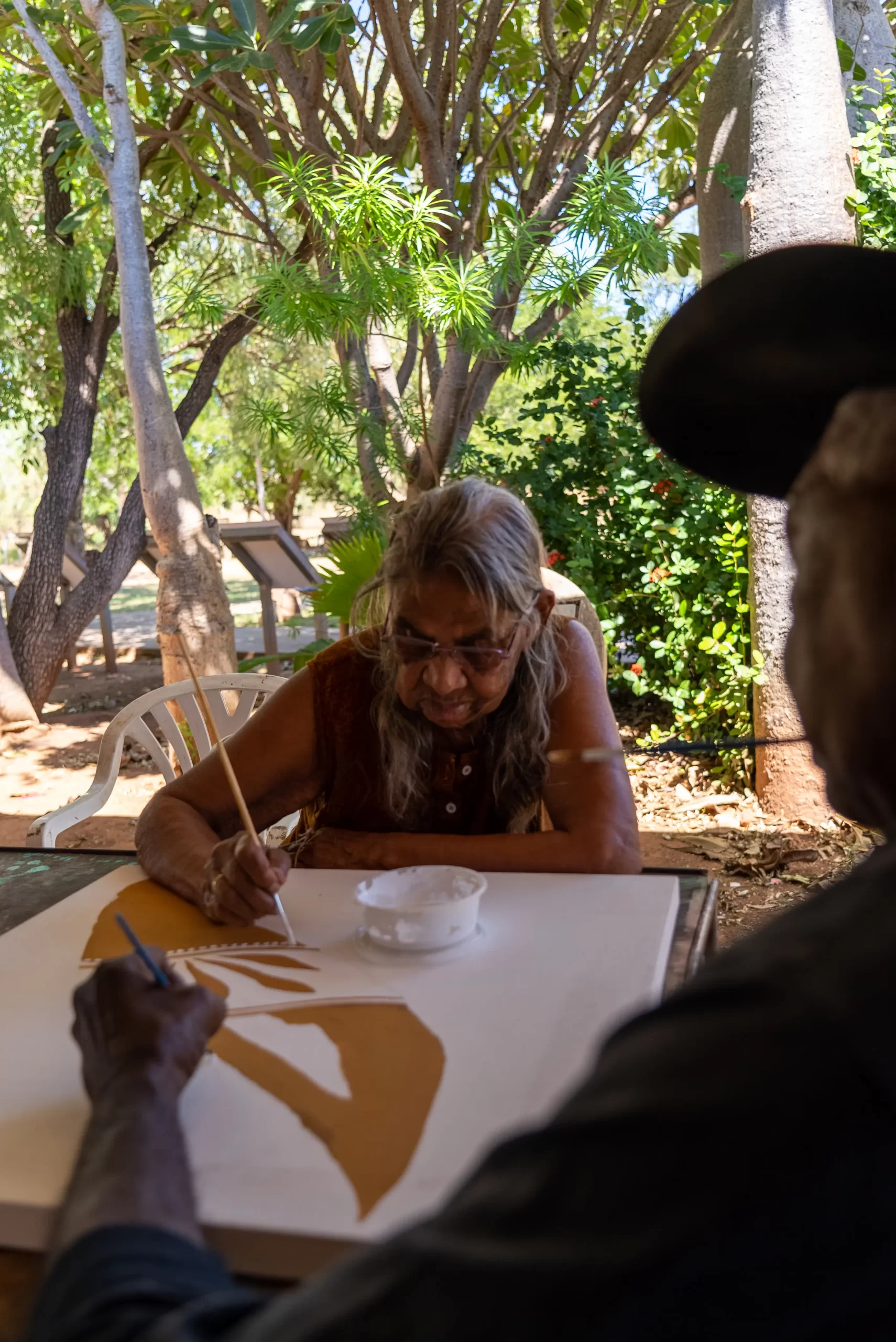 Two people painting on a canvas in a tropical area