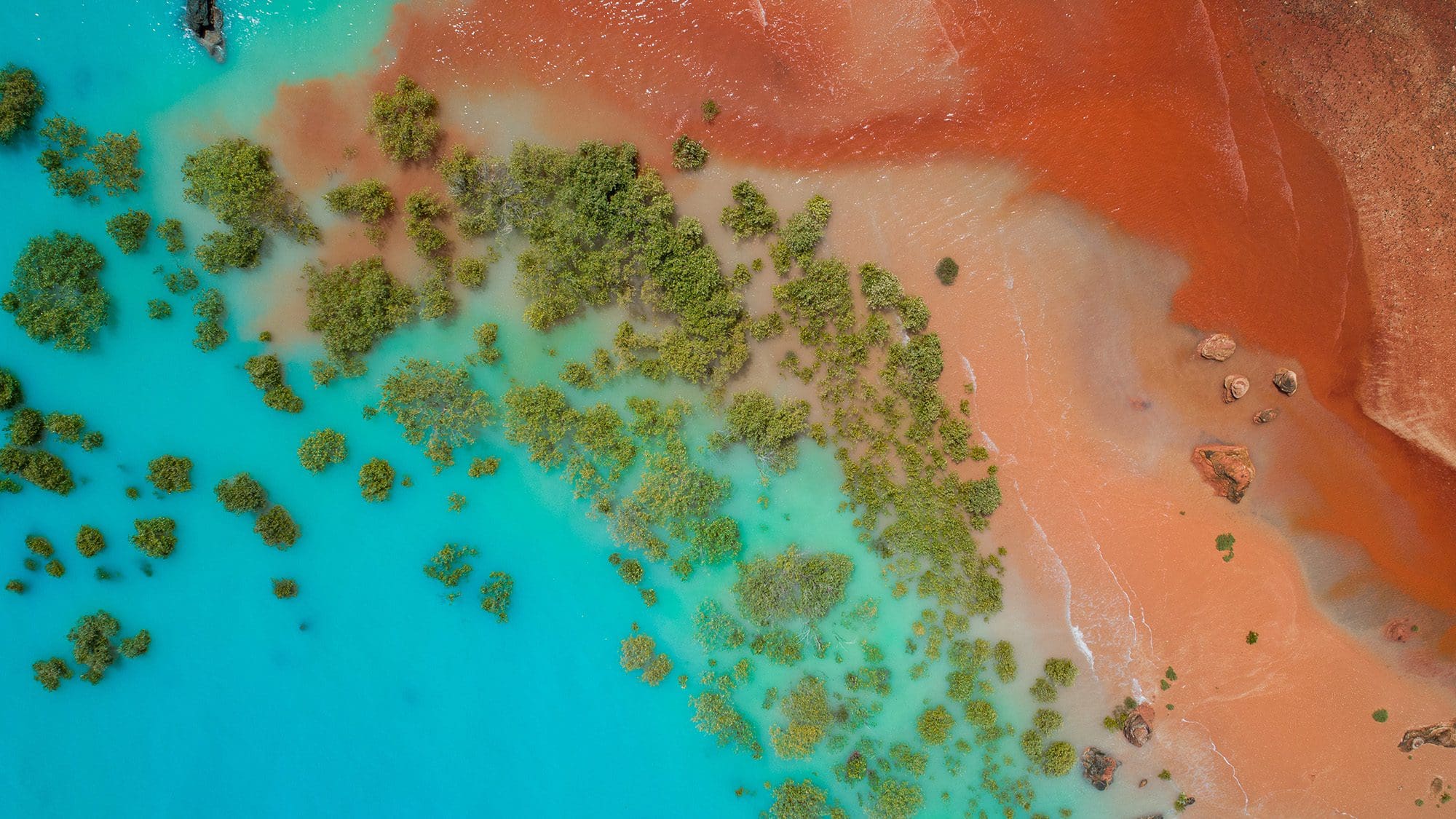 Aerial view of turquoise ocean water meeting red dirt shoreline