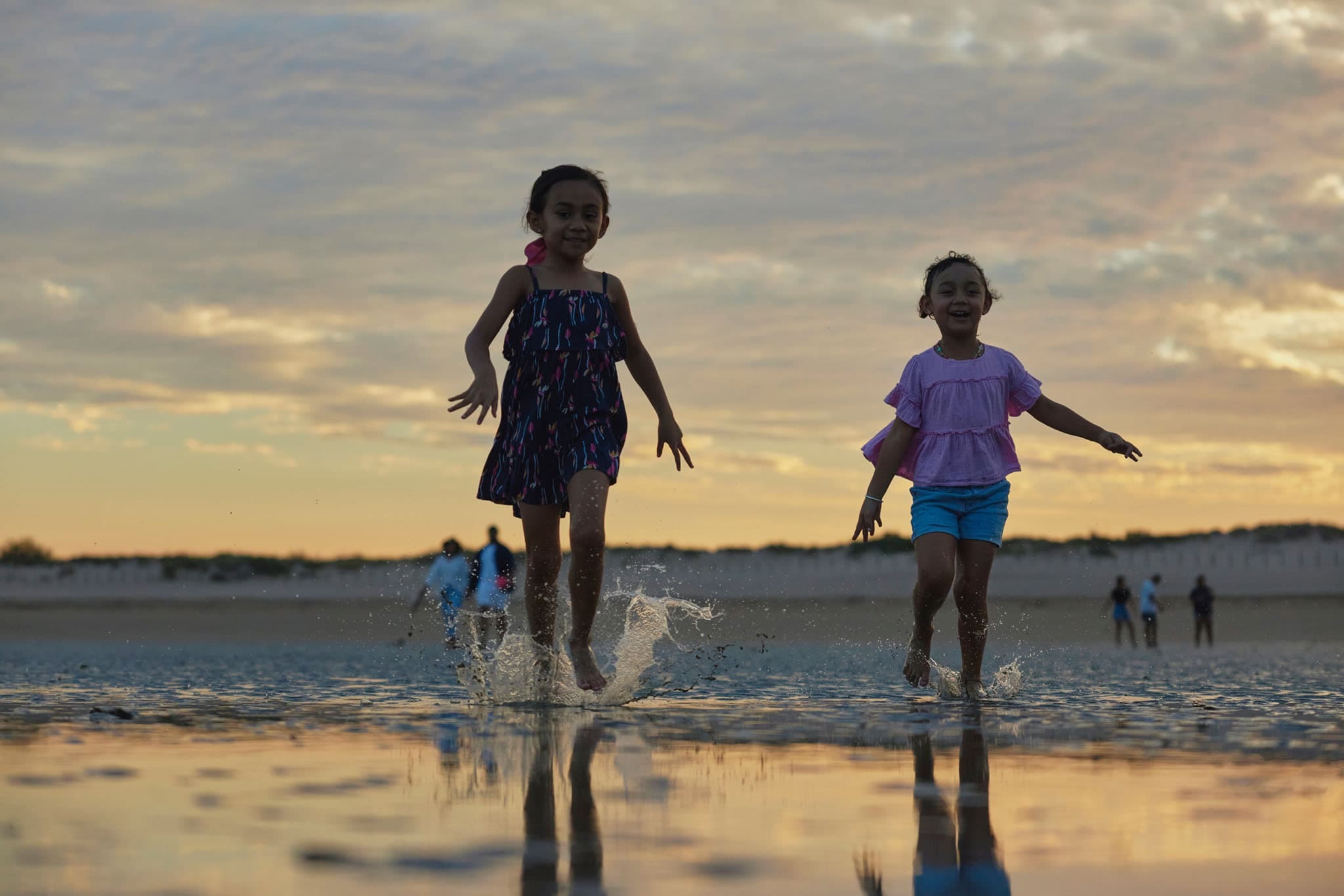 Two children running in shallow water as the sun sets in Karratha