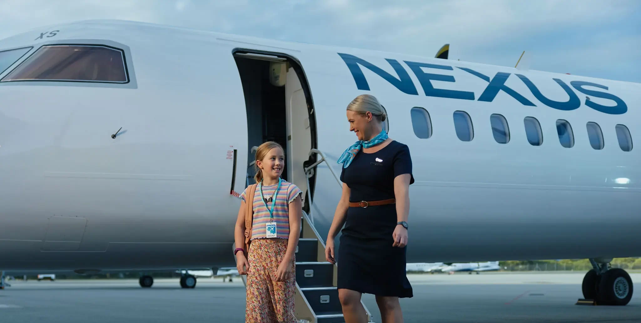 Flight hostess smiling at a young girl in front of a Nexus Airlines airplane
