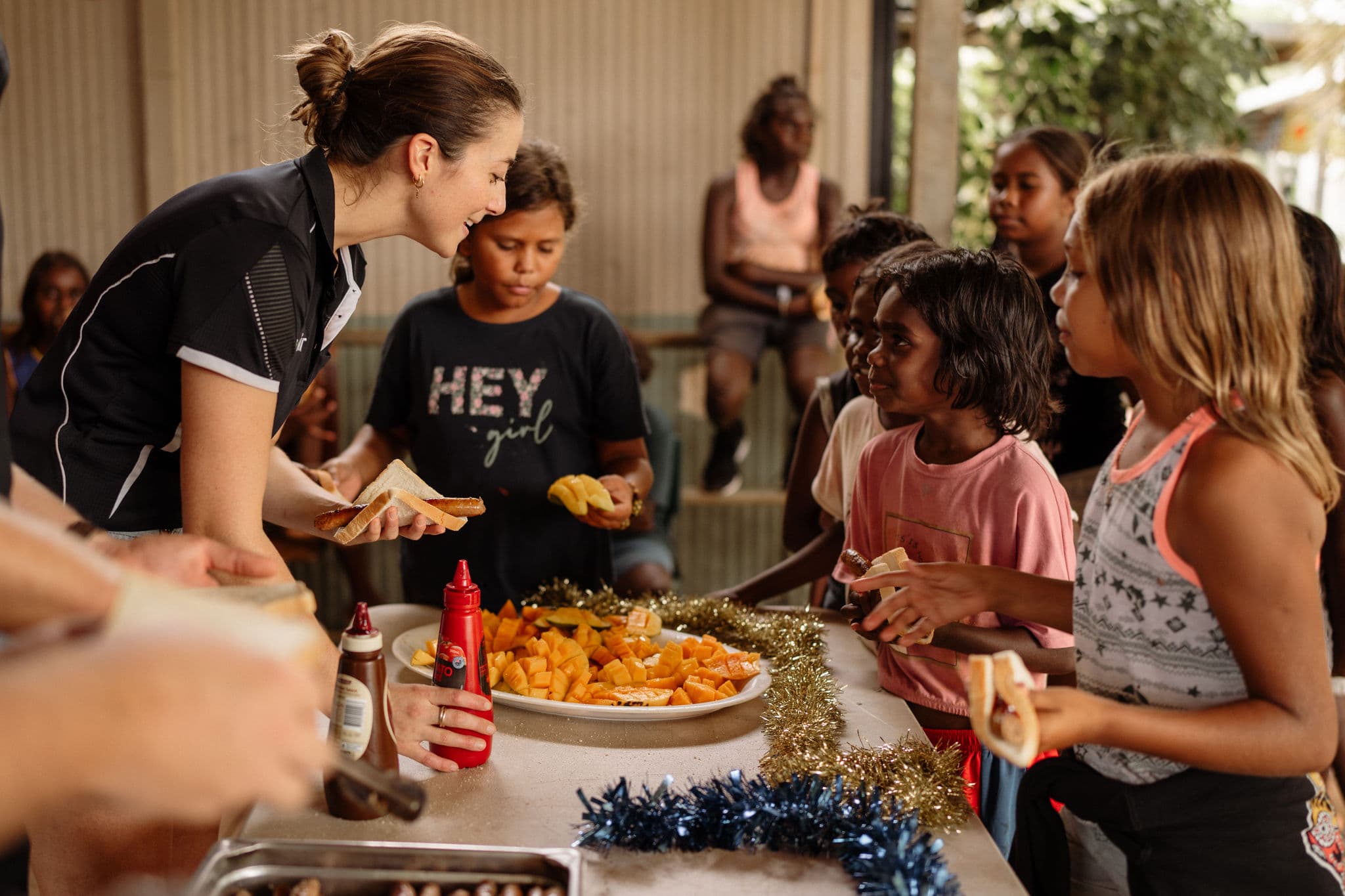 Woman serving sausages in bread and mango to a group of children